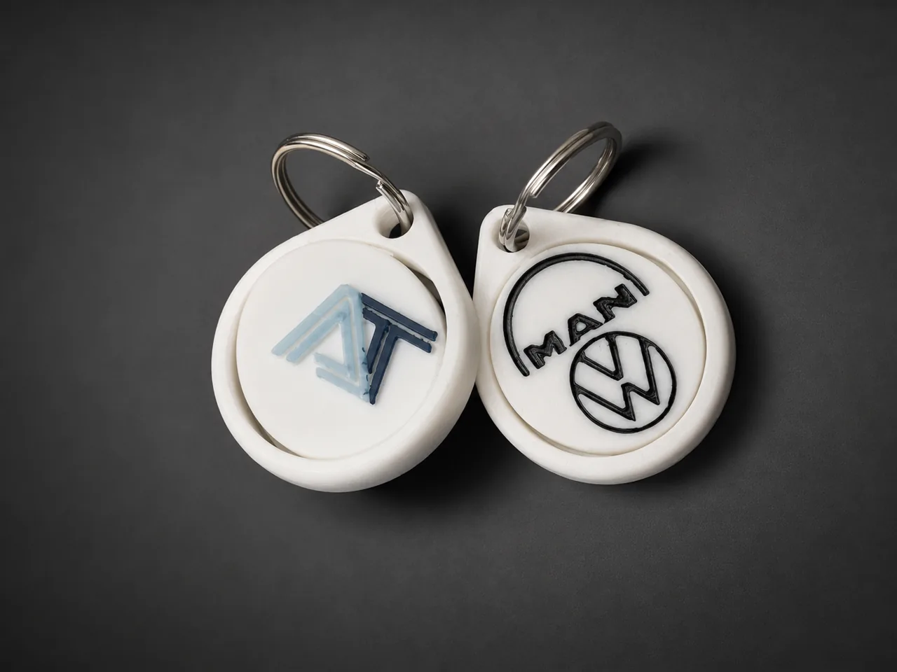 Los dos llaveros VW MAN impresos en 3D en blanco: uno con el logo AT del cliente en azul, el otro con el logo MAN VW en negro