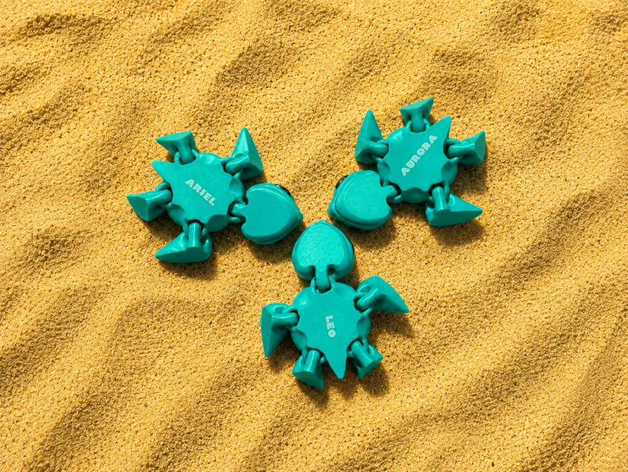 Tres tortugas impresas en verde azulado sobre arena, cada una con un nombre distinto grabado con láser: Ariel, Aurora y Leo