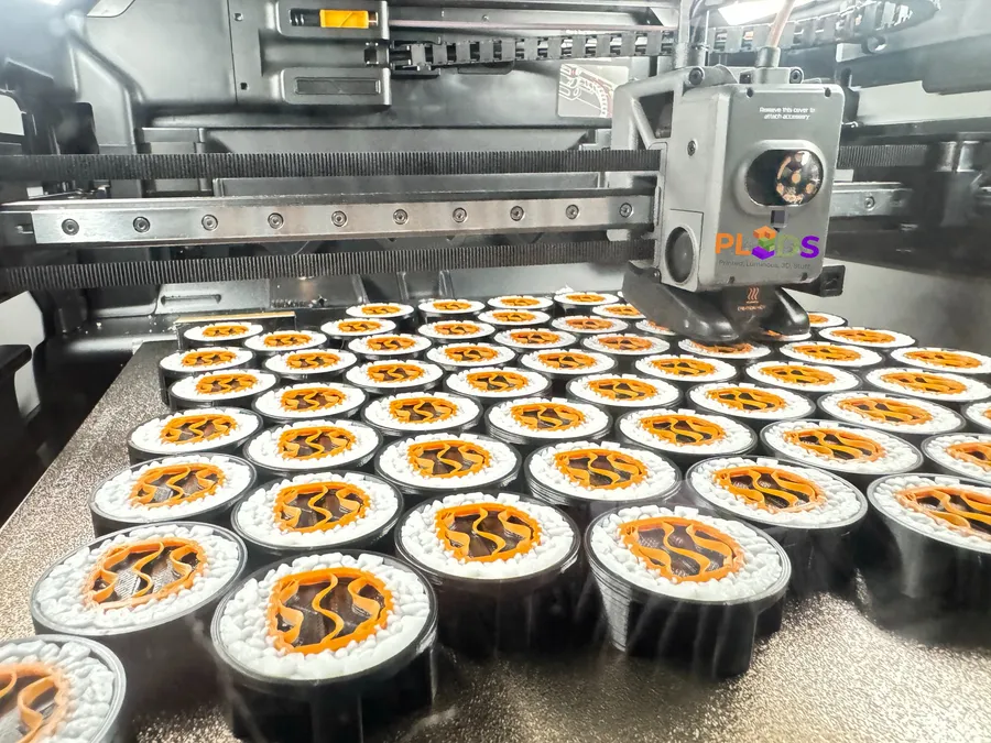 Cama de impresión llena de piezas circulares idénticas con el logo de PL3DS a color